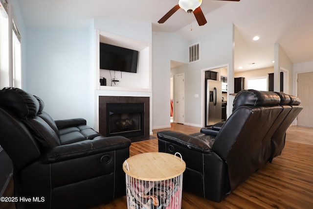 living room with wood finished floors, visible vents, a ceiling fan, vaulted ceiling, and a tiled fireplace