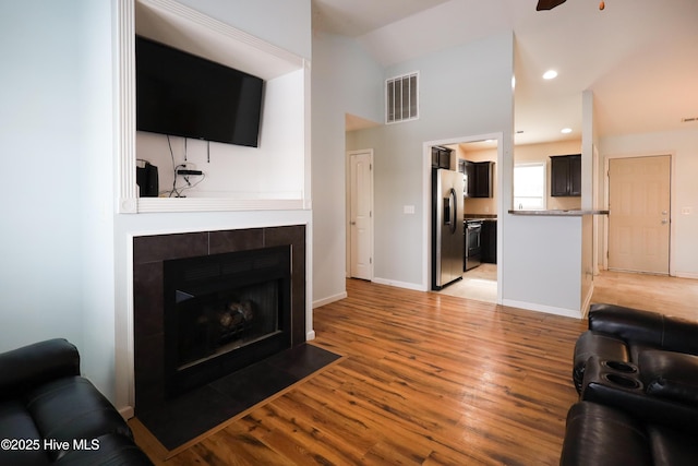 living room with a tile fireplace, ceiling fan, and light wood-type flooring