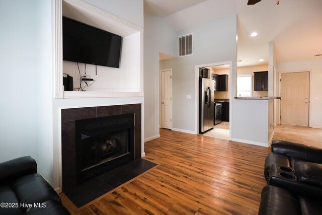 living room featuring baseboards, visible vents, a tiled fireplace, and light wood finished floors