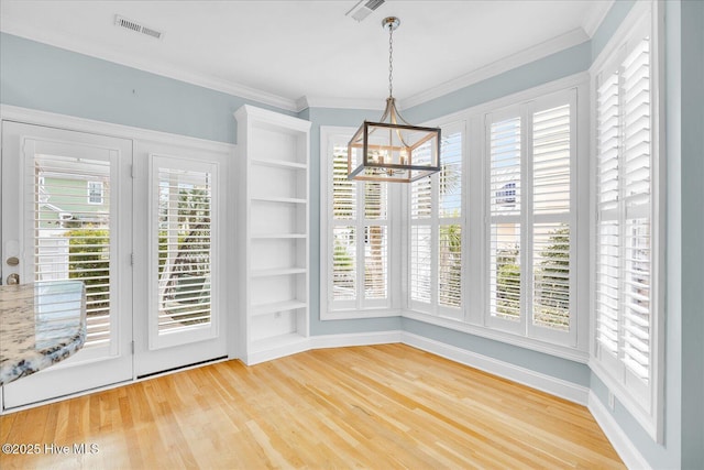 unfurnished dining area with built in features, a chandelier, ornamental molding, and hardwood / wood-style floors