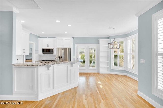 kitchen with appliances with stainless steel finishes, white cabinetry, hanging light fixtures, light hardwood / wood-style flooring, and ornamental molding