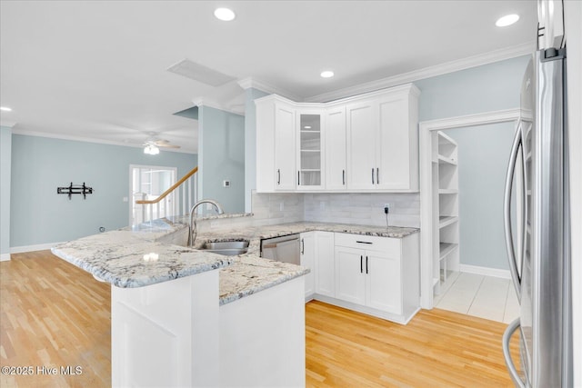 kitchen featuring kitchen peninsula, white cabinets, tasteful backsplash, light wood-type flooring, and stainless steel appliances