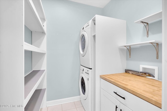 laundry area with stacked washer / dryer, cabinets, and light tile patterned floors