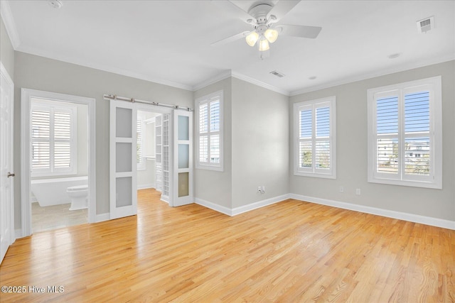 spare room with ornamental molding, light hardwood / wood-style floors, ceiling fan, and a barn door