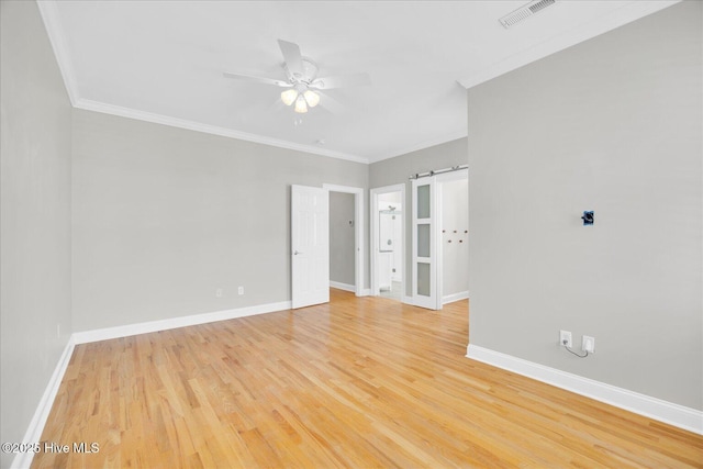 unfurnished room with ornamental molding, ceiling fan, a barn door, and light hardwood / wood-style flooring