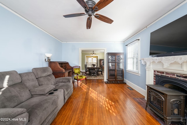 living room featuring ornamental molding, a wood stove, hardwood / wood-style floors, and ceiling fan