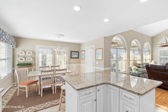 kitchen with a notable chandelier, light stone countertops, hanging light fixtures, white cabinets, and a kitchen island