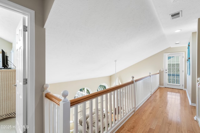 corridor featuring light wood-type flooring, a textured ceiling, and lofted ceiling