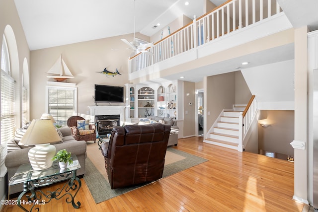 living room with built in shelves, hardwood / wood-style floors, high vaulted ceiling, and ceiling fan