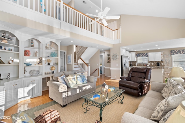 living room with ceiling fan, sink, light wood-type flooring, a towering ceiling, and built in shelves