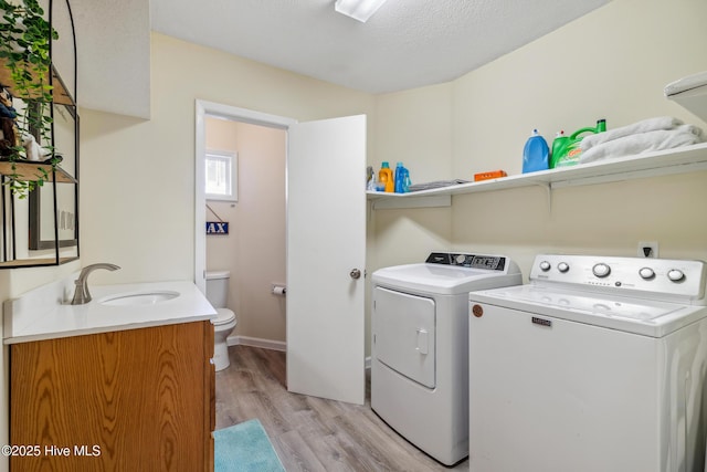 laundry room featuring a textured ceiling, sink, washing machine and dryer, and light wood-type flooring