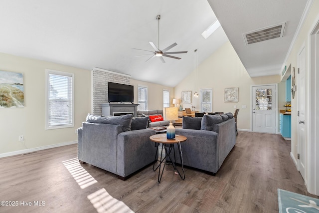 living room with ceiling fan, a skylight, high vaulted ceiling, wood-type flooring, and a fireplace