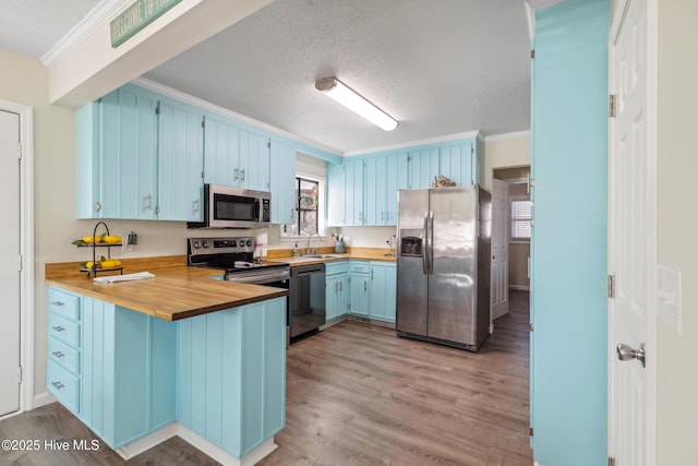 kitchen featuring appliances with stainless steel finishes, kitchen peninsula, crown molding, blue cabinetry, and light hardwood / wood-style flooring