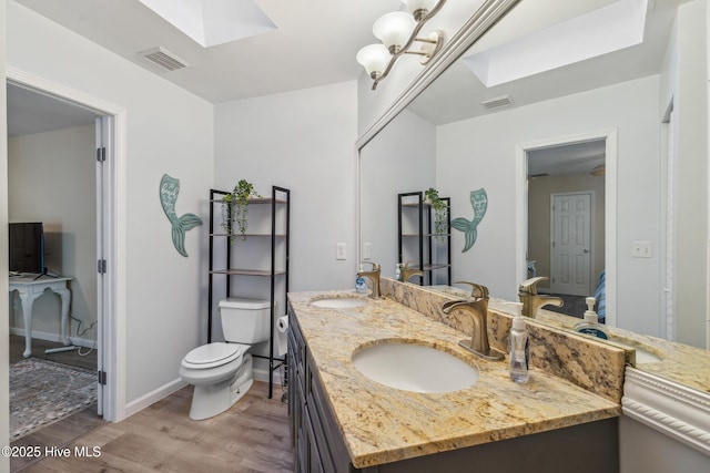 bathroom featuring a skylight, hardwood / wood-style flooring, vanity, a notable chandelier, and toilet