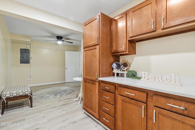 kitchen featuring ceiling fan, electric panel, light stone countertops, and light wood-type flooring