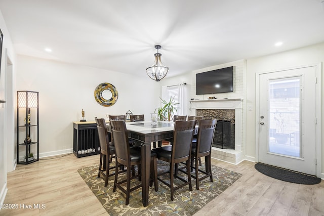 dining space with a chandelier, a brick fireplace, and light hardwood / wood-style flooring