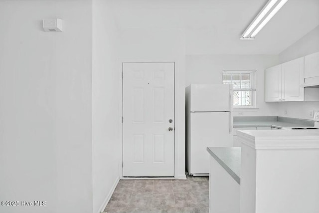 kitchen featuring light countertops, freestanding refrigerator, white cabinetry, and range