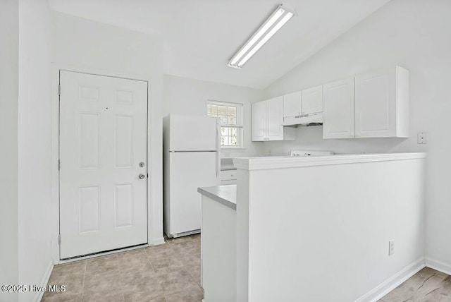 kitchen with lofted ceiling, light countertops, freestanding refrigerator, white cabinets, and under cabinet range hood