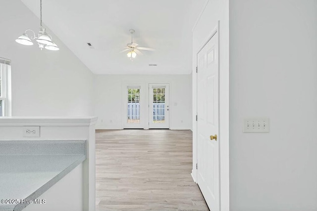 unfurnished living room featuring ceiling fan with notable chandelier, lofted ceiling, light wood-style flooring, and baseboards