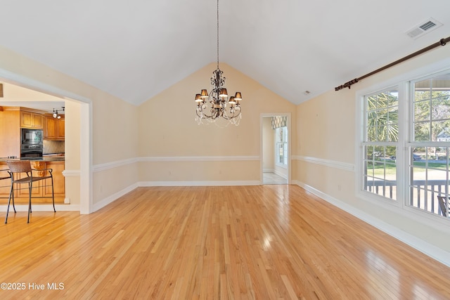 unfurnished dining area featuring plenty of natural light, a chandelier, vaulted ceiling, and light wood-type flooring