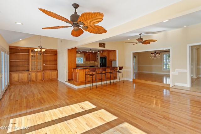 unfurnished living room featuring ceiling fan with notable chandelier, lofted ceiling, light hardwood / wood-style floors, and built in features