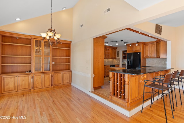 kitchen featuring a breakfast bar area, dark stone counters, kitchen peninsula, black fridge, and light wood-type flooring