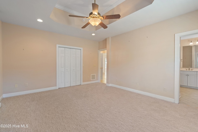 unfurnished bedroom with ensuite bathroom, sink, a tray ceiling, light carpet, and a closet