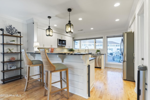 kitchen featuring white cabinetry, kitchen peninsula, stainless steel appliances, crown molding, and light wood-type flooring