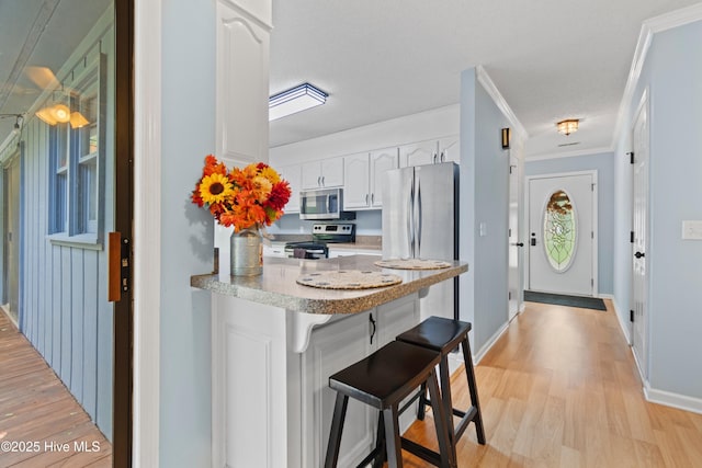 kitchen with light hardwood / wood-style flooring, white cabinetry, ornamental molding, a breakfast bar area, and stainless steel appliances