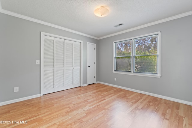 unfurnished bedroom featuring light wood-type flooring, crown molding, a textured ceiling, and a closet