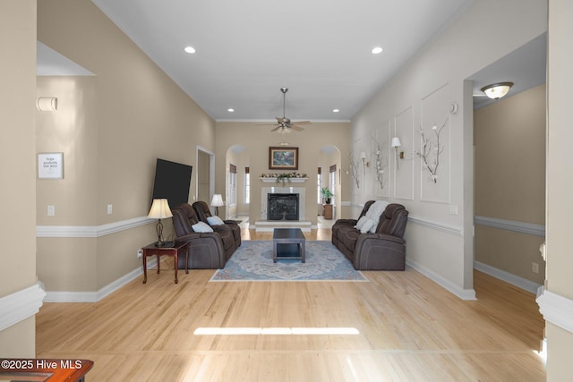 living area featuring baseboards, arched walkways, a ceiling fan, and a fireplace with raised hearth