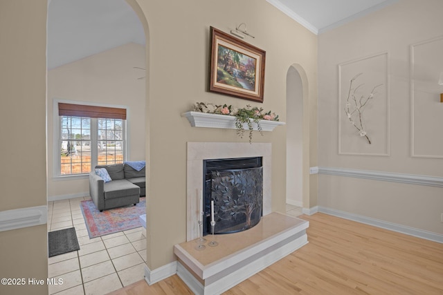 room details featuring a fireplace with raised hearth, baseboards, arched walkways, ornamental molding, and wood finished floors