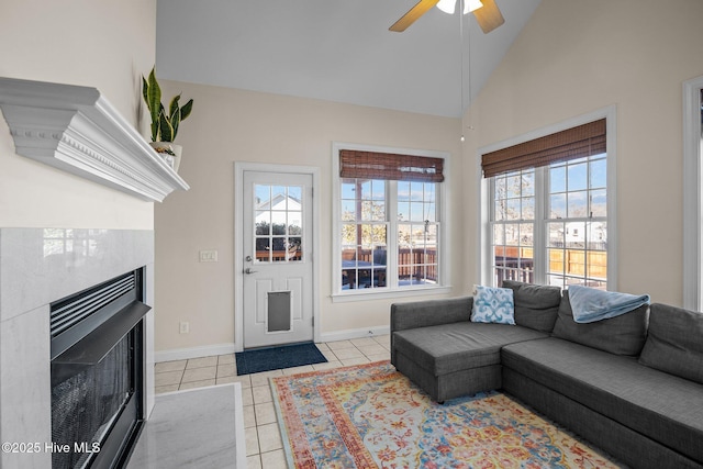 living area featuring a fireplace with flush hearth, baseboards, tile patterned floors, a ceiling fan, and high vaulted ceiling