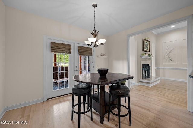 dining area with a chandelier, a fireplace with raised hearth, baseboards, light wood-type flooring, and french doors