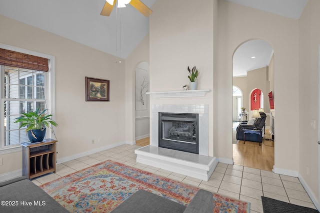 living room with ceiling fan, a premium fireplace, high vaulted ceiling, and light tile patterned floors