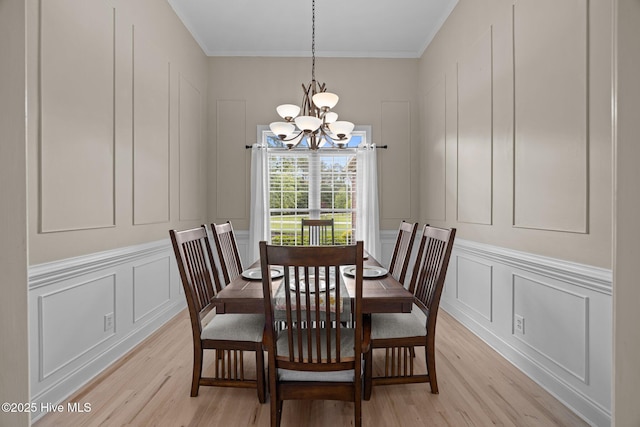 dining room with an inviting chandelier, a decorative wall, crown molding, and light wood finished floors