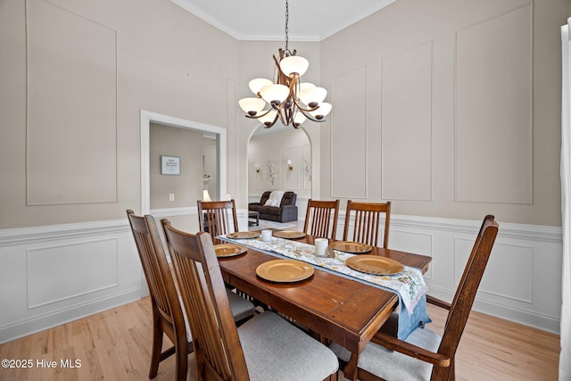dining space featuring arched walkways, ornamental molding, light wood-style flooring, and a decorative wall