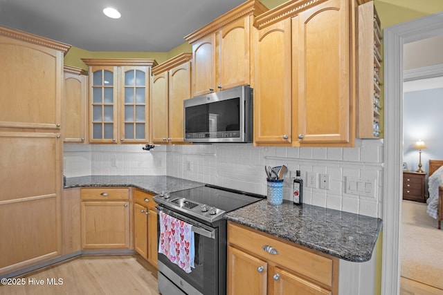 kitchen featuring appliances with stainless steel finishes, light hardwood / wood-style flooring, decorative backsplash, and dark stone countertops