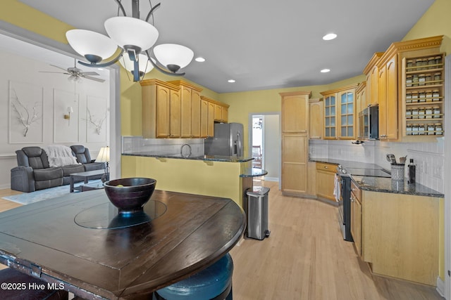 kitchen featuring decorative light fixtures, light wood-type flooring, dark stone counters, stainless steel appliances, and backsplash