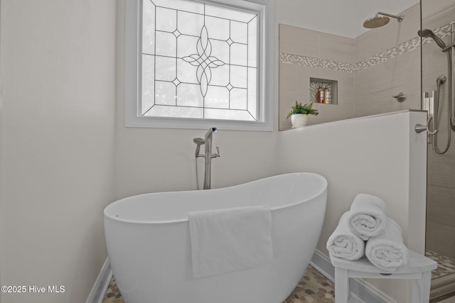 full bath featuring a tile shower, a freestanding tub, and baseboards