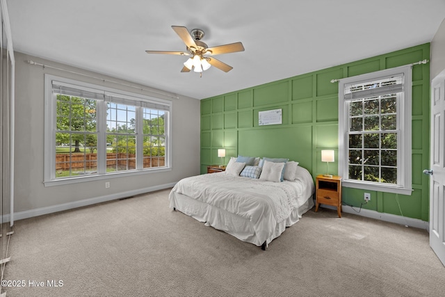 carpeted bedroom with a decorative wall, a ceiling fan, and baseboards