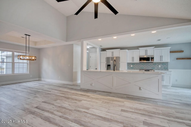 kitchen featuring ceiling fan with notable chandelier, backsplash, white cabinets, stainless steel appliances, and light wood-type flooring