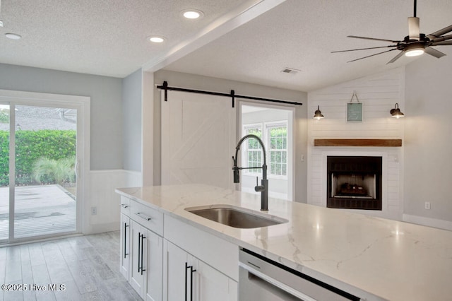 kitchen with sink, white cabinets, stainless steel dishwasher, light stone countertops, and a textured ceiling