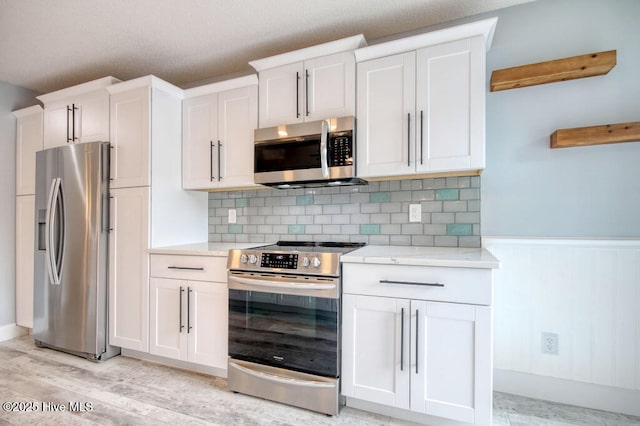 kitchen featuring tasteful backsplash, appliances with stainless steel finishes, white cabinets, and light hardwood / wood-style flooring