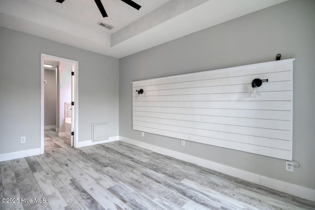 empty room with light hardwood / wood-style flooring, a raised ceiling, and ceiling fan