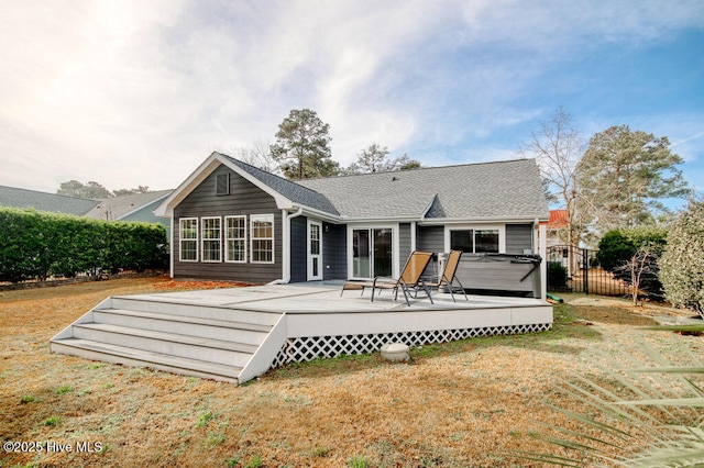 rear view of house with a hot tub, a deck, and a lawn