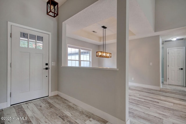 foyer with a raised ceiling, a chandelier, and light wood-type flooring