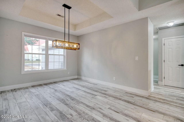 unfurnished room with a raised ceiling, light hardwood / wood-style floors, and a textured ceiling