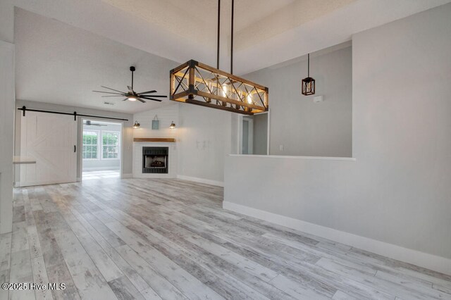 unfurnished living room with ceiling fan, a barn door, vaulted ceiling, and light hardwood / wood-style flooring