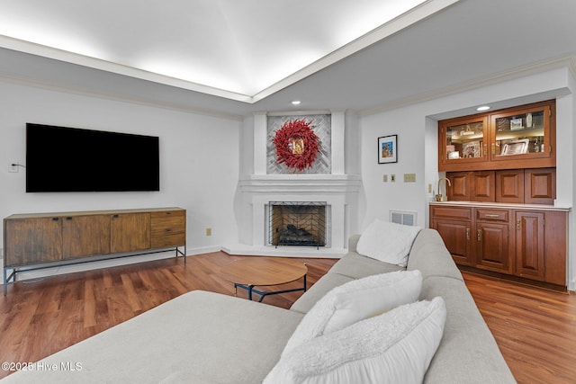 living room featuring crown molding, a large fireplace, hardwood / wood-style floors, and bar area